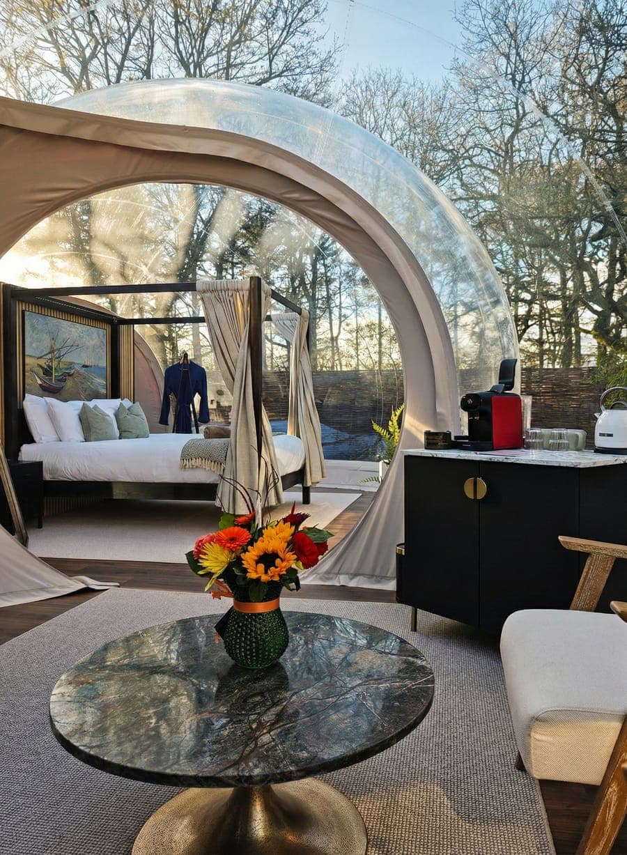 Inside the dome — four-poster bed, marble table with fresh flowers, and evening light through the transparent walls