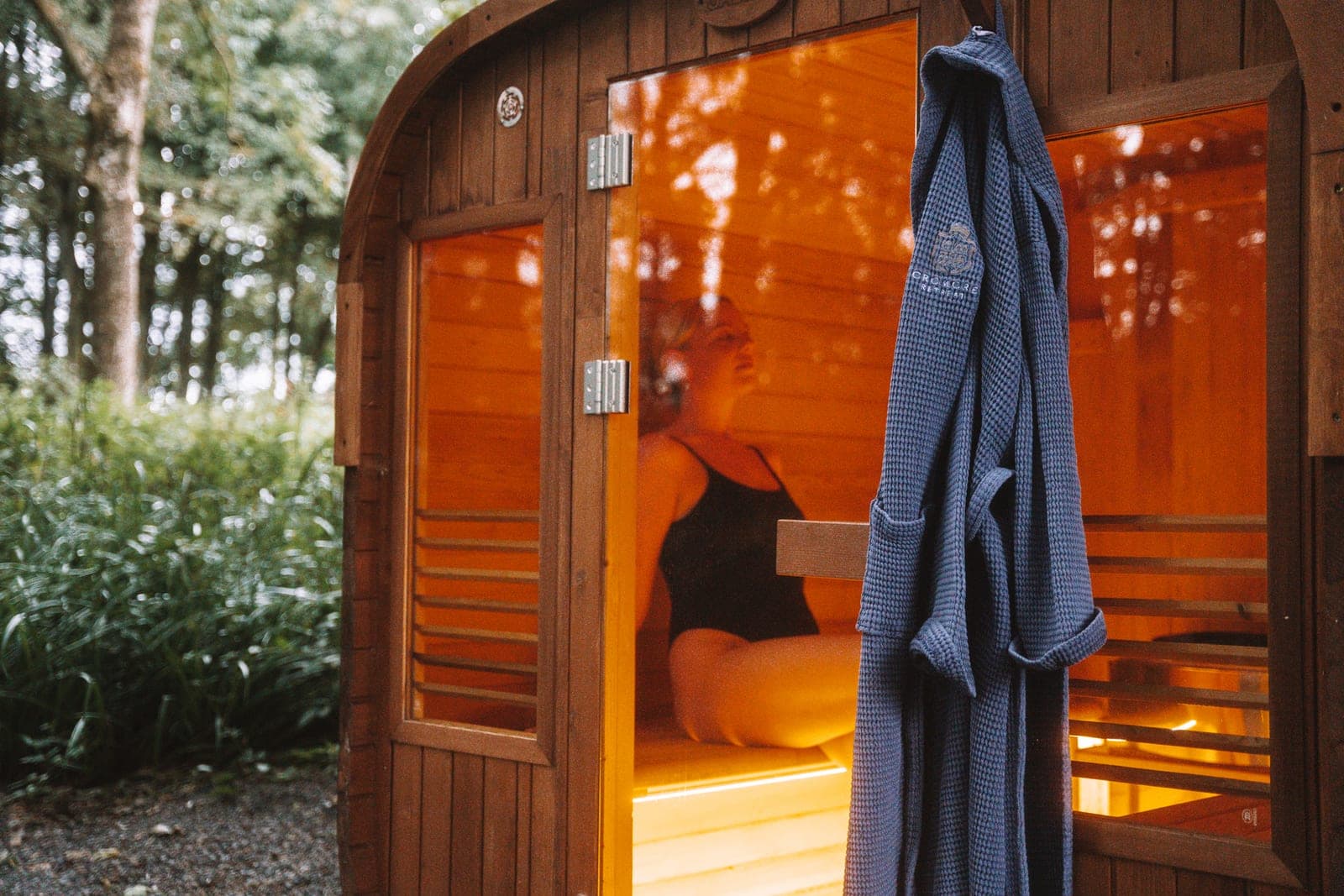 Guest relaxing inside the glowing woodland sauna, a Cromore Retreat robe hanging by the door